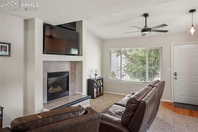 Living area featuring carpet flooring, ceiling fan, a tiled fireplace, baseboards, and a textured ceiling
