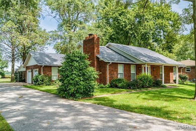 Ranch-style house featuring a driveway, brick siding, a chimney, and a front yard