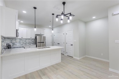 Kitchen with pendant lighting, light hardwood / wood-style flooring, appliances with stainless steel finishes, and white cabinets