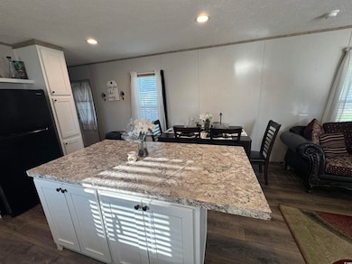 Kitchen with freestanding refrigerator, a textured ceiling, dark wood-type flooring, white cabinets, and a kitchen island
