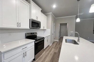 Kitchen with appliances with stainless steel finishes, crown molding, wood finished floors, white cabinetry, and decorative light fixtures