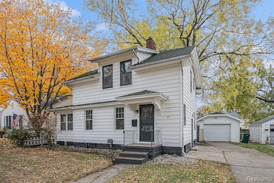 View of front facade with an outbuilding, a garage, a chimney, concrete driveway, and roof with shingles