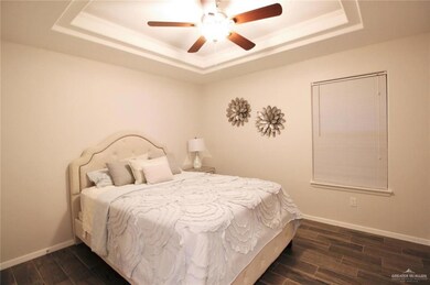 Bedroom with a raised ceiling, dark wood-style flooring, and ceiling fan
