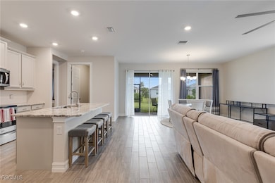 Kitchen with open floor plan, recessed lighting, a kitchen island with sink, light wood-type flooring, and light stone counters