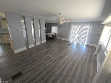 Unfurnished living room featuring dark wood-type flooring, a ceiling fan, baseboards, and plenty of natural light