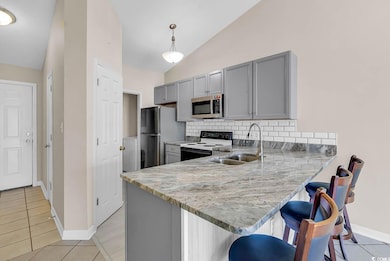 Kitchen with gray cabinetry, a kitchen bar, light tile patterned floors, a peninsula, and stainless steel appliances