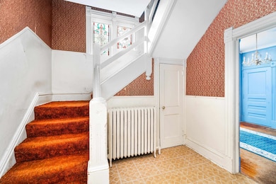 Stairs featuring wallpapered walls, radiator heating unit, wainscoting, and a chandelier
