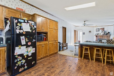 Kitchen with freestanding refrigerator, ornamental molding, a kitchen breakfast bar, dark wood-style floors, and brown cabinetry