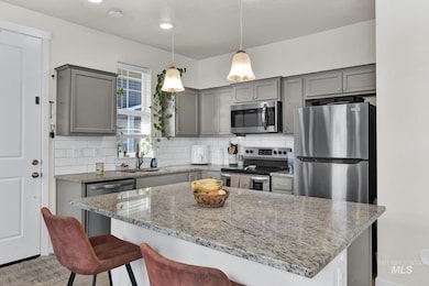 Kitchen featuring appliances with stainless steel finishes, gray cabinets, a kitchen breakfast bar, and light stone counters