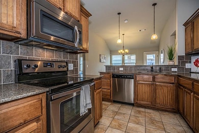 Kitchen with appliances with stainless steel finishes, a sink, vaulted ceiling, decorative backsplash, and a chandelier