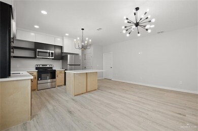 Kitchen with appliances with stainless steel finishes, a chandelier, a kitchen island, light wood-style flooring, and hanging light fixtures