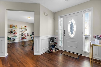 Foyer entrance with dark wood-style flooring, wainscoting, and a decorative wall