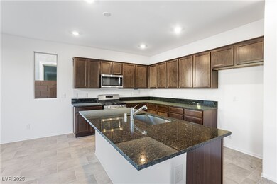 Kitchen with dark stone counters, dark brown cabinetry, appliances with stainless steel finishes, a kitchen island with sink, and recessed lighting