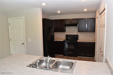 Kitchen with black appliances, sink, dark brown cabinetry, and dark wood-type flooring