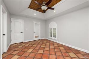 Unfurnished room with a tray ceiling, light tile patterned floors, a ceiling fan, and baseboards