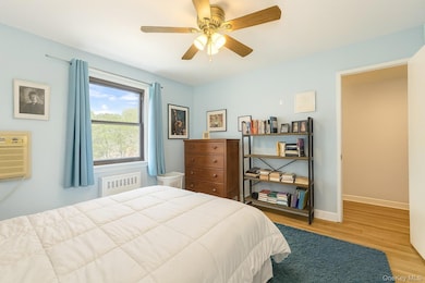Bedroom featuring wood finished floors, radiator heating unit, ceiling fan, and a wall mounted air conditioner