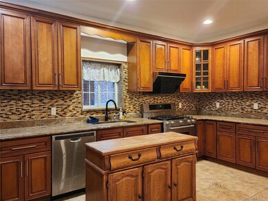 Kitchen featuring brown cabinets, stainless steel appliances, backsplash, range hood, and recessed lighting
