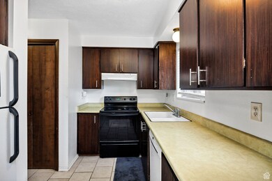 Kitchen featuring white appliances, light countertops, light tile patterned flooring, dark brown cabinets, and under cabinet range hood