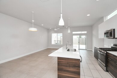 Open concept kitchen and living space with modern finishes, large windows for natural light, and contemporary lighting fixtures. The kitchen features stainless steel appliances, a central island with a sink, and ample cabinet space.