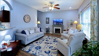 Living room with wood finished floors, baseboards, a fireplace with raised hearth, arched walkways, and ceiling fan