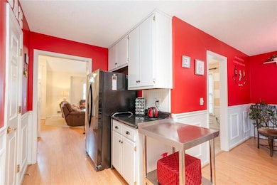 Kitchen with freestanding refrigerator, light wood-style floors, white cabinets, wainscoting, and a textured ceiling