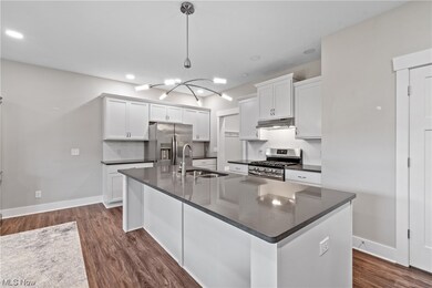 Large kitchen island with sink, appliances with stainless steel finishes, white cabinetry, luxury vinyl plank flooring, and quartz countertops.