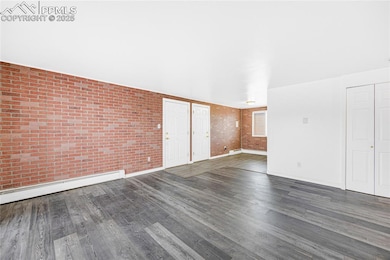 Unfurnished living room featuring dark wood-type flooring, brick wall, and a baseboard radiator