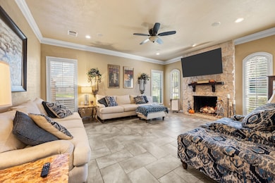 Living area featuring crown molding, plenty of natural light, a stone fireplace, and ceiling fan