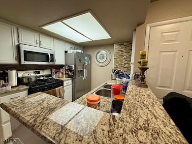 Kitchen featuring white cabinets, light stone coun