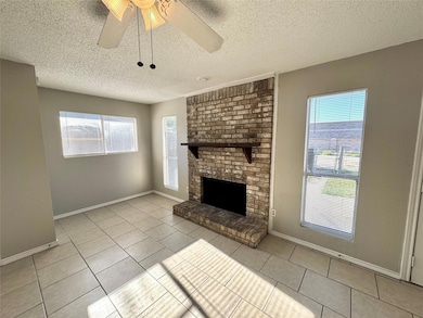 Unfurnished living room with ceiling fan, a textured ceiling, a fireplace, and light tile patterned floors