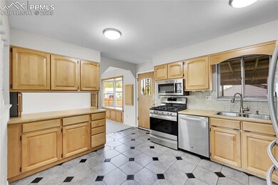 Kitchen with stainless steel appliances, a sink, light brown cabinets, tasteful backsplash, and light countertops