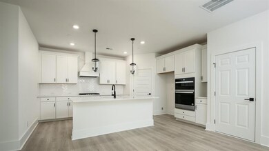 Kitchen featuring custom exhaust hood, multiple ovens, light wood-style flooring, tasteful backsplash, and white cabinets