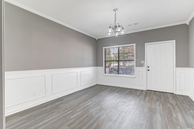 Unfurnished dining area with a chandelier, wainscoting, a decorative wall, ornamental molding, and wood finished floors