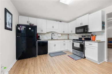 Kitchen with black appliances, light wood-style flooring, and decorative backsplash