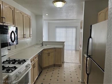 Kitchen with stove, black refrigerator, light countertops, a textured ceiling, and stainless steel microwave