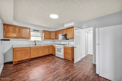 Kitchen featuring white appliances, dark wood finished floors, light countertops, and brown cabinetry
