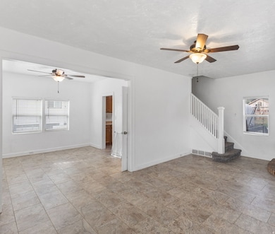 Unfurnished living room featuring ceiling fan, plenty of natural light, a textured ceiling, and stairway