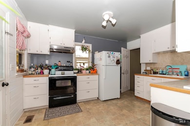 Kitchen with black / electric stove, white cabinets, backsplash, and freestanding refrigerator