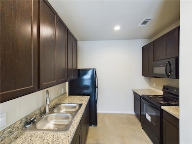 Kitchen featuring dark brown cabinetry, light ston