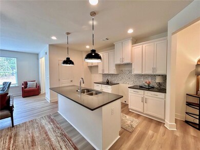 Kitchen with a sink, dark countertops, light wood finished floors, white cabinetry, and an island with sink