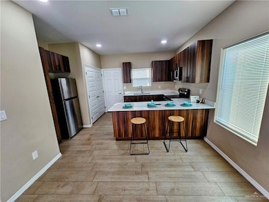 Kitchen featuring light wood finished floors, light countertops, stainless steel appliances, a peninsula, and visible vents