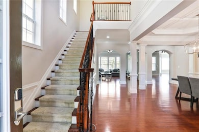 Foyer featuring wood finished floors, stairs, arched walkways, a high ceiling, and ornamental molding