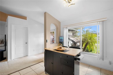 Kitchen featuring wood counters, light tile patterned floors, lofted ceiling, a center island, and dark cabinets