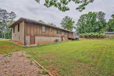 Back of property with board and batten siding, brick siding, a wooden deck, and central AC