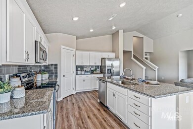 Kitchen featuring stainless steel appliances, white cabinetry, vaulted ceiling, a textured ceiling, and light wood finished floors