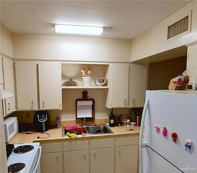 Kitchen featuring white appliances, a textured ceiling, and range hood