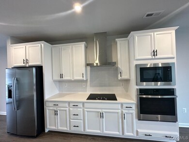 Kitchen with visible vents, decorative backsplash, wall chimney range hood, white cabinets, and appliances with stainless steel finishes