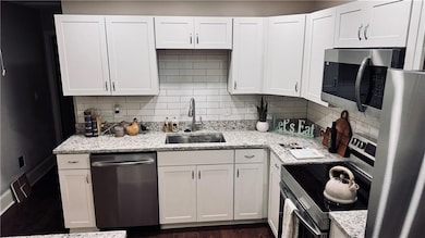Kitchen with appliances with stainless steel finishes, decorative backsplash, white cabinets, and light stone countertops