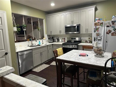 Kitchen with stainless steel appliances, a sink, gray cabinets, dark wood finished floors, and light countertops
