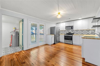 Kitchen with stainless steel appliances, ornamental molding, light wood-type flooring, tasteful backsplash, and white cabinets